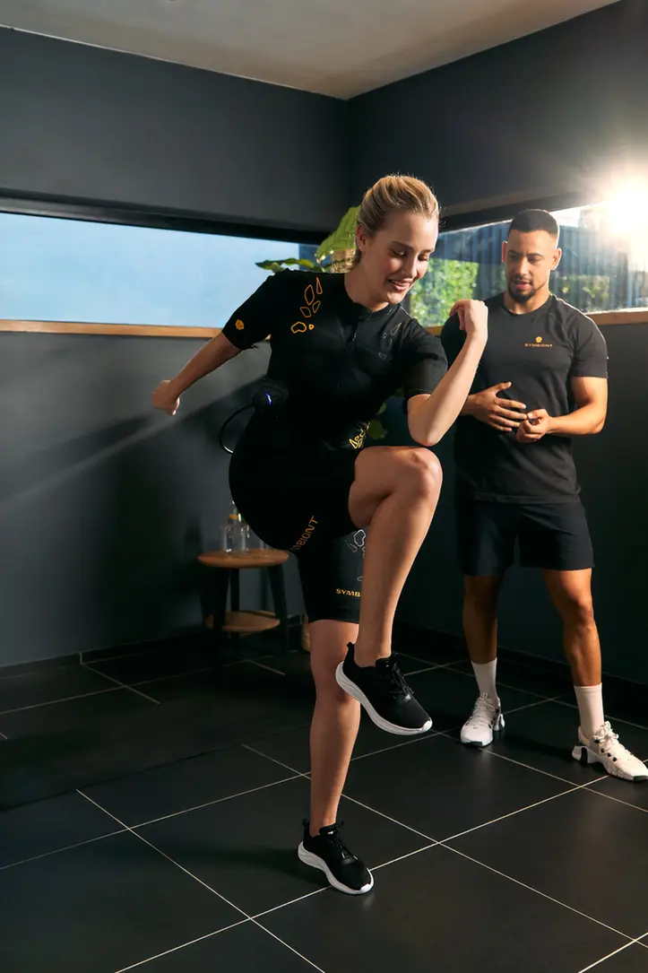 Experience SYMBIONT EMS Training at Your Local EMS Studio Personal trainer guiding a client in a SYMBIONT EMS suit during a trial session at a local EMS studio. Experience personalized training, guidance, and motivation in your EMS trial.