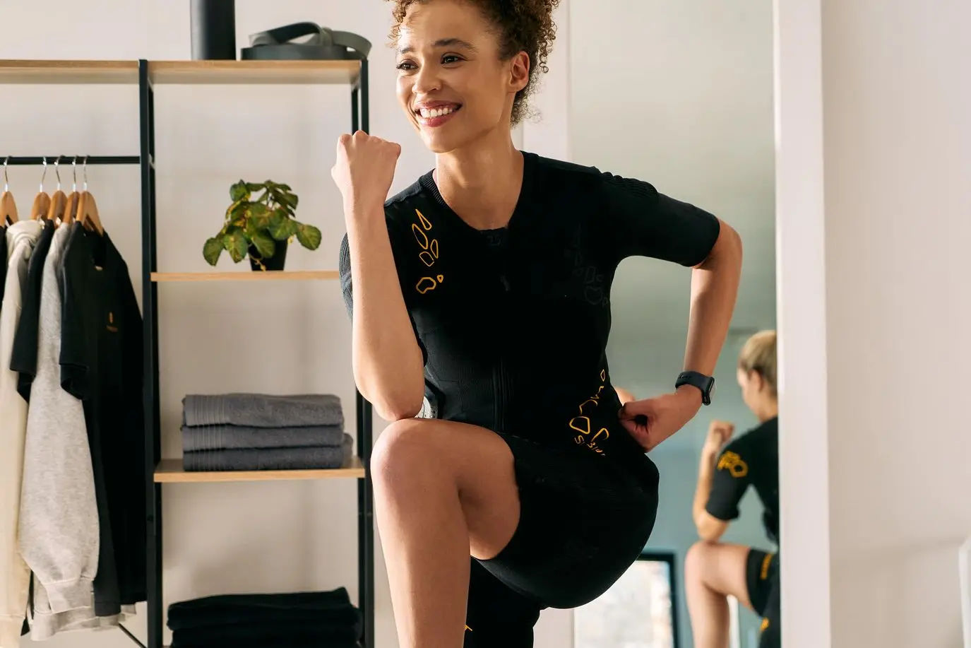 Person smiling and performing a dynamic exercise in the SYMBIOMT EMS suit , showcasing the flexibility and happiness of EMS training.