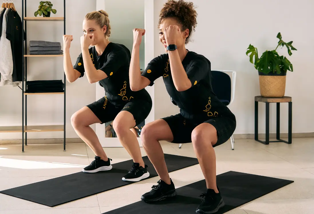 Fast results with EMS training in Cape Town Two women in EMS suits do squats and use EMS training in Cape Town to get quick results in a short time.
